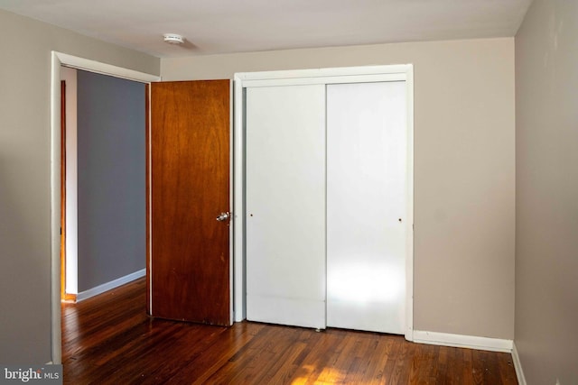 unfurnished bedroom with a closet, baseboards, and hardwood / wood-style flooring