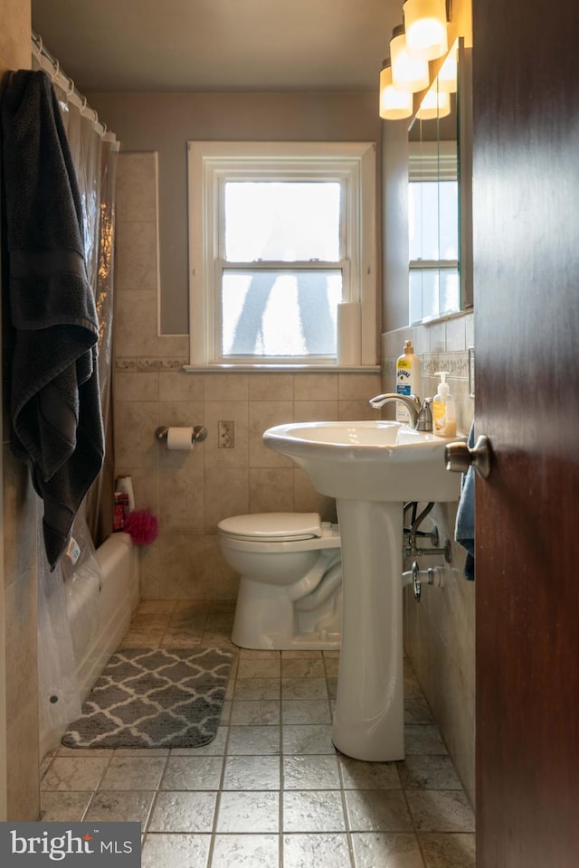 full bath with a shower with shower curtain, toilet, tile walls, and stone tile flooring