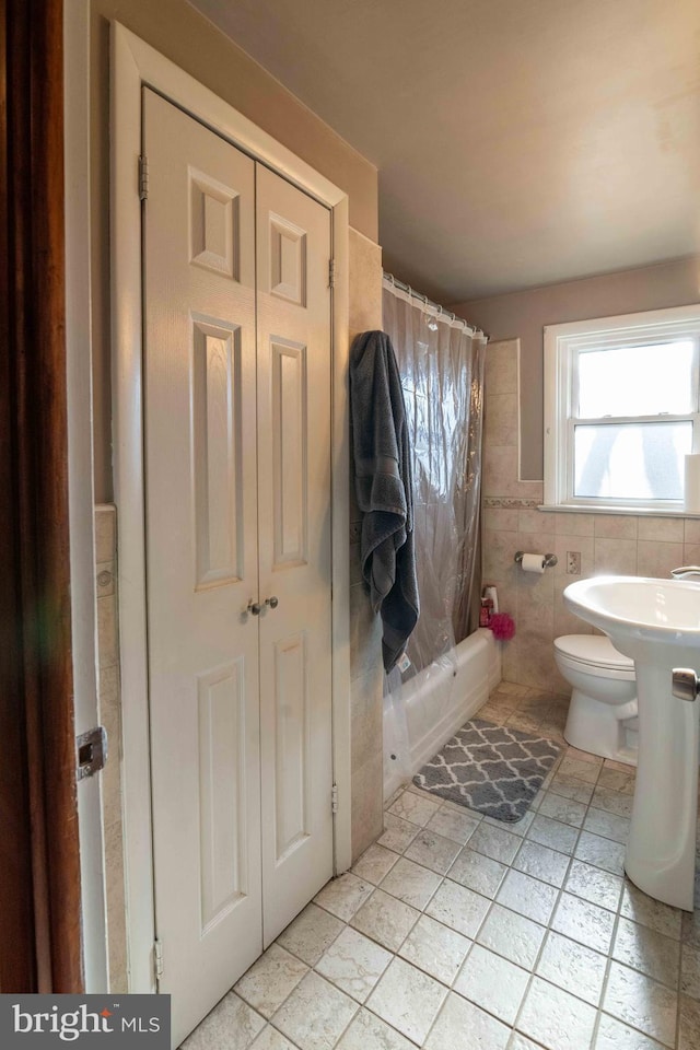 bathroom featuring a wainscoted wall, toilet, tile walls, and shower / bath combo with shower curtain