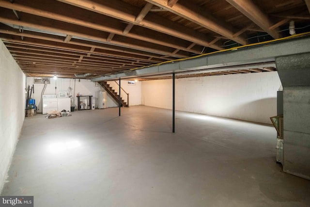 unfinished basement featuring stairs, concrete block wall, water heater, and washer and clothes dryer