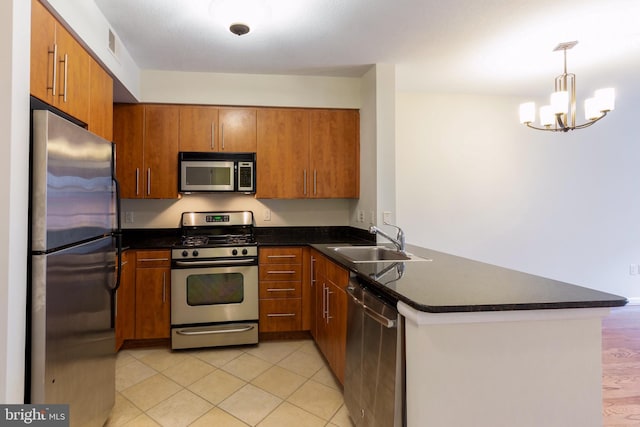 kitchen featuring dark countertops, appliances with stainless steel finishes, brown cabinets, a peninsula, and a sink