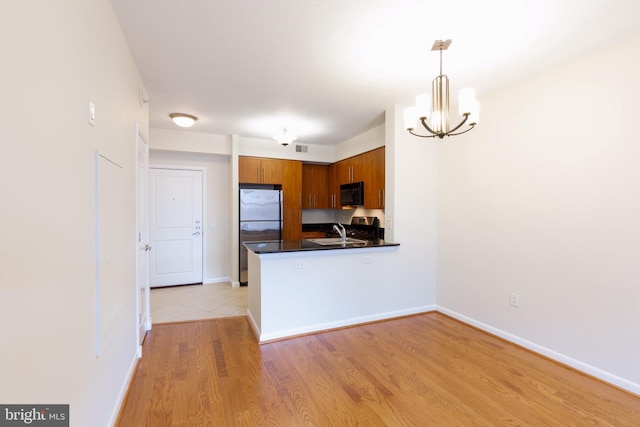 kitchen with dark countertops, appliances with stainless steel finishes, brown cabinets, a peninsula, and light wood-style floors