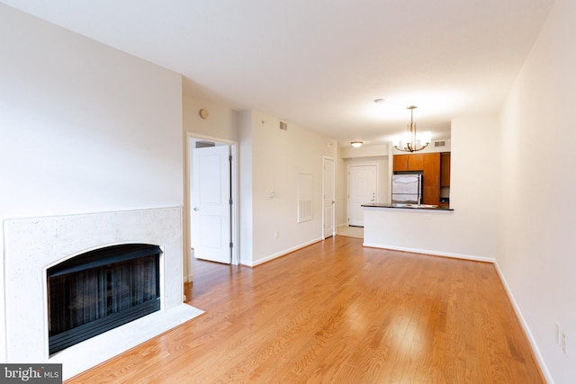 unfurnished living room with visible vents, baseboards, light wood-style flooring, a fireplace with flush hearth, and a chandelier