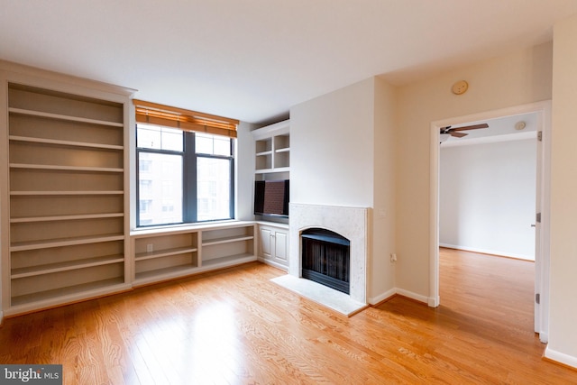 unfurnished living room featuring a ceiling fan, a tile fireplace, baseboards, and light wood finished floors