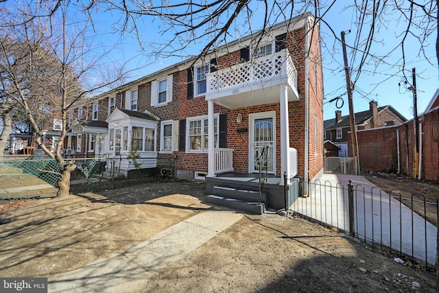 view of property featuring a balcony, a gate, fence, and brick siding