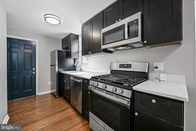 kitchen with stainless steel appliances, dark wood-type flooring, a sink, dark cabinetry, and baseboards