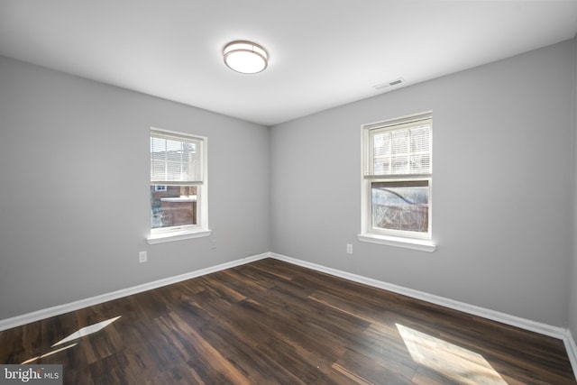 unfurnished room featuring dark wood-style floors, visible vents, and baseboards