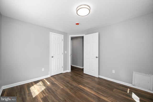 unfurnished bedroom featuring baseboards, dark wood finished floors, and a closet