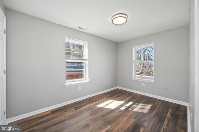 unfurnished room featuring baseboards, visible vents, and dark wood finished floors