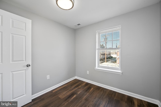 unfurnished room featuring dark wood-style floors, visible vents, and baseboards