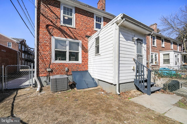 rear view of house with a chimney, entry steps, a gate, central AC, and fence