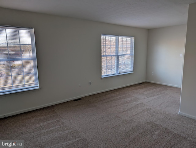 carpeted spare room featuring visible vents, a healthy amount of sunlight, and baseboards