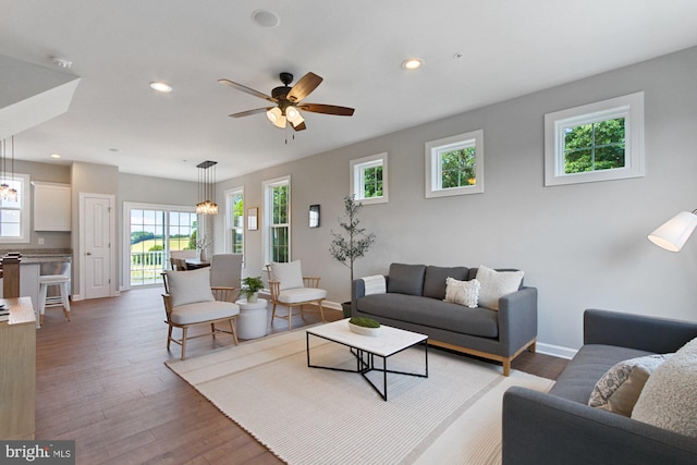 living room featuring light wood-style floors, recessed lighting, baseboards, and ceiling fan with notable chandelier