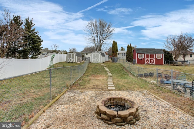 view of yard featuring an outbuilding, a fenced backyard, a fire pit, and a storage unit