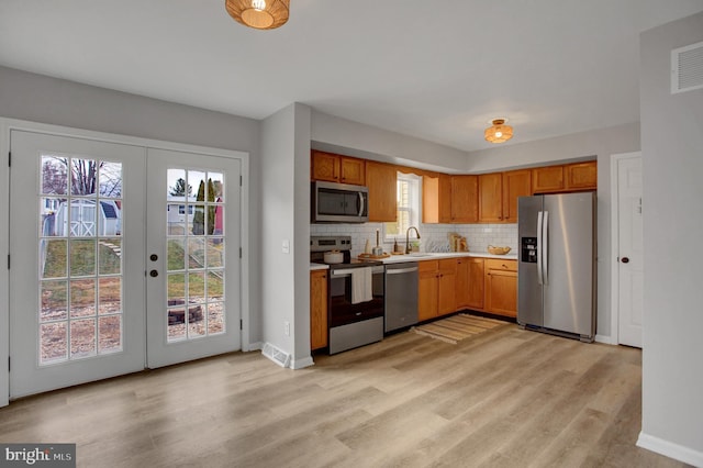 kitchen featuring decorative backsplash, stainless steel appliances, french doors, light wood-type flooring, and a sink