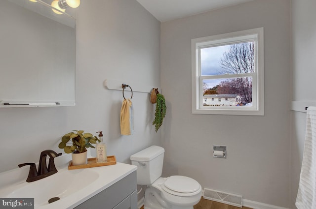 half bath with toilet, vanity, visible vents, and baseboards