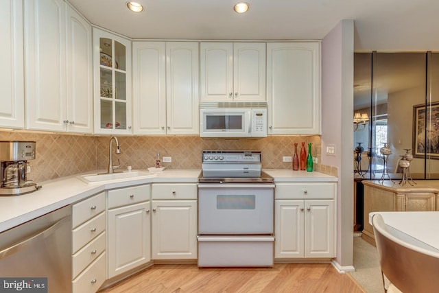 kitchen with light wood-style flooring, white appliances, a sink, white cabinets, and light countertops