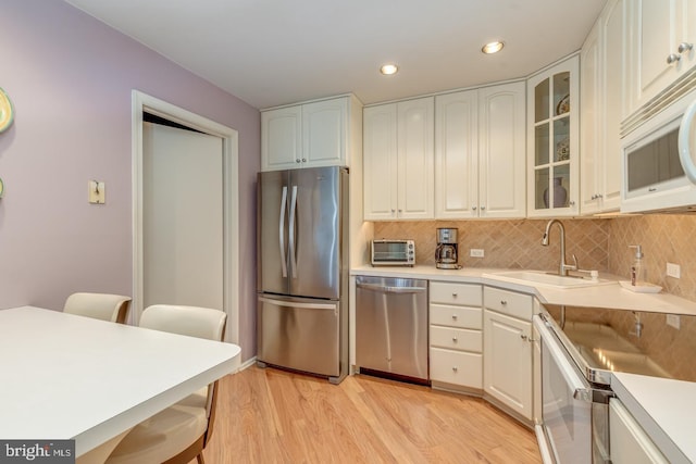 kitchen featuring appliances with stainless steel finishes, backsplash, a sink, and light wood-style floors