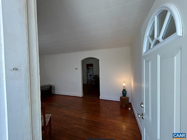 corridor featuring dark wood-type flooring, arched walkways, and baseboards