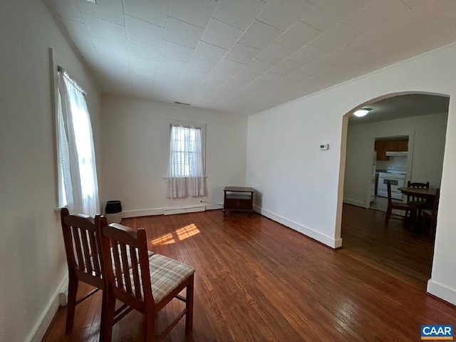 sitting room featuring arched walkways, wood-type flooring, visible vents, a baseboard heating unit, and baseboards