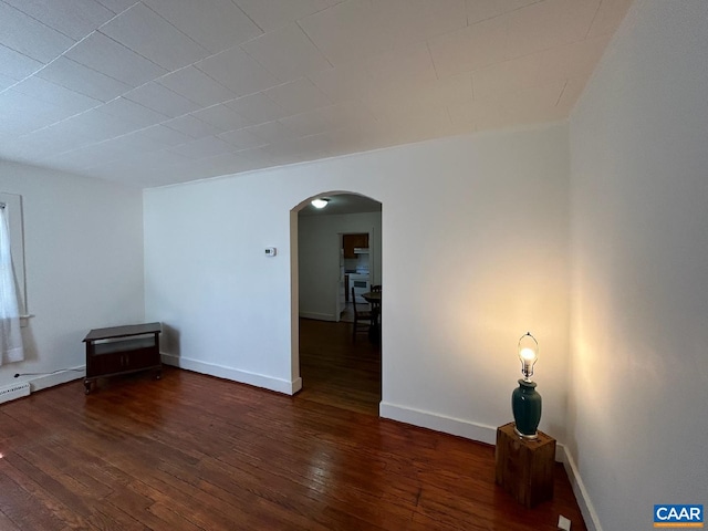 empty room featuring dark wood-type flooring, arched walkways, and baseboards