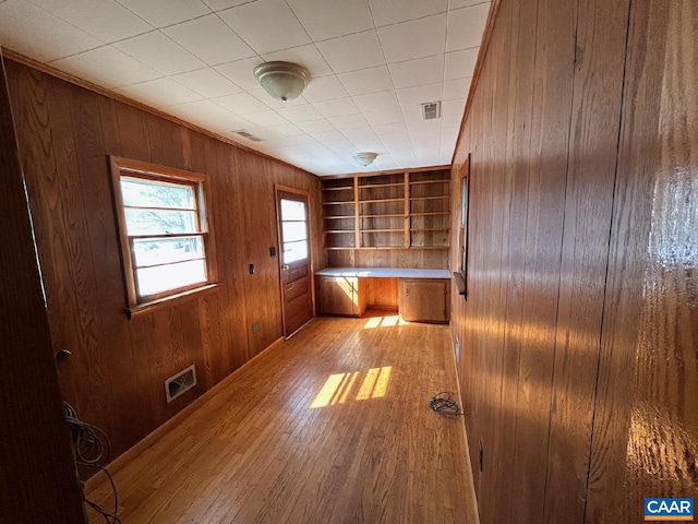 interior space featuring wooden walls, light wood-type flooring, visible vents, and built in desk