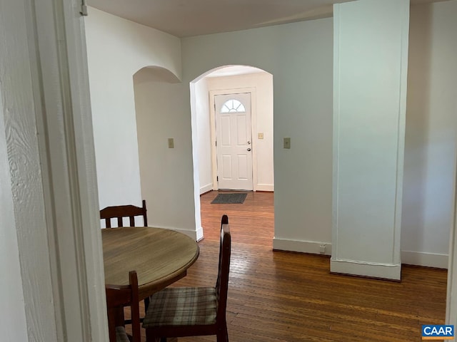 dining room featuring baseboards, arched walkways, and dark wood finished floors