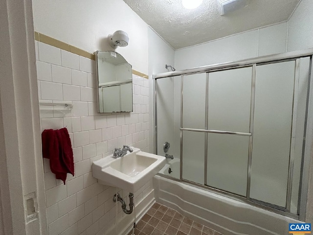 full bath with tile walls, combined bath / shower with glass door, a sink, a textured ceiling, and tile patterned flooring