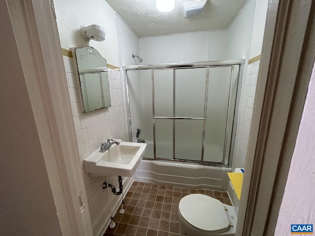 full bath featuring tile walls, bath / shower combo with glass door, backsplash, a textured ceiling, and tile patterned floors