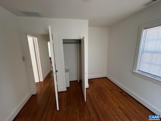 unfurnished bedroom featuring baseboards, a closet, visible vents, and wood finished floors