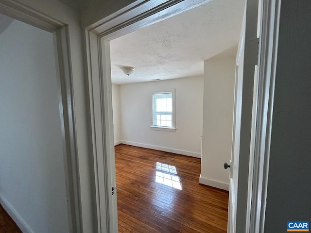 empty room with a textured ceiling, dark wood-style flooring, and baseboards