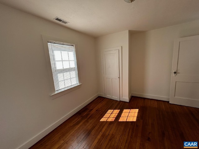 unfurnished bedroom with baseboards, visible vents, dark wood finished floors, and a textured ceiling