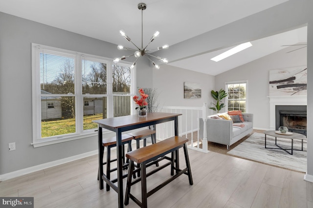 dining area with baseboards, lofted ceiling, light wood-type flooring, a fireplace, and a chandelier