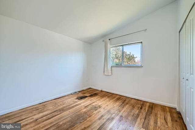 unfurnished bedroom featuring a closet, visible vents, vaulted ceiling, wood finished floors, and baseboards