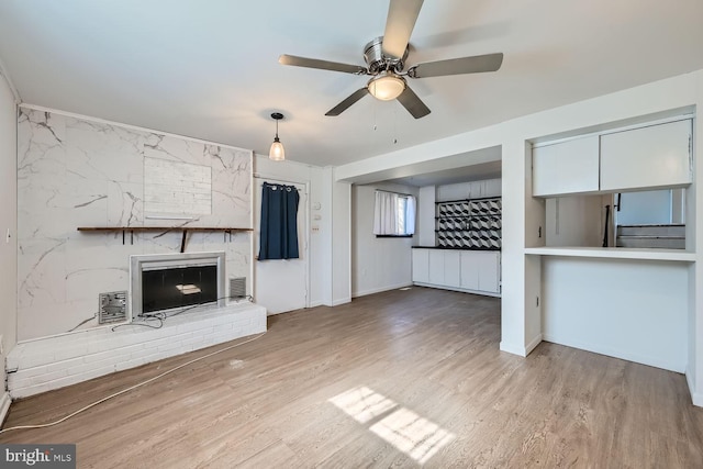 unfurnished living room with a brick fireplace, ceiling fan, visible vents, and wood finished floors