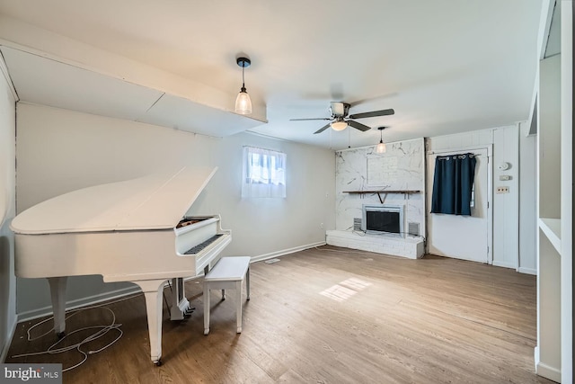 living area with a ceiling fan, a large fireplace, baseboards, and wood finished floors