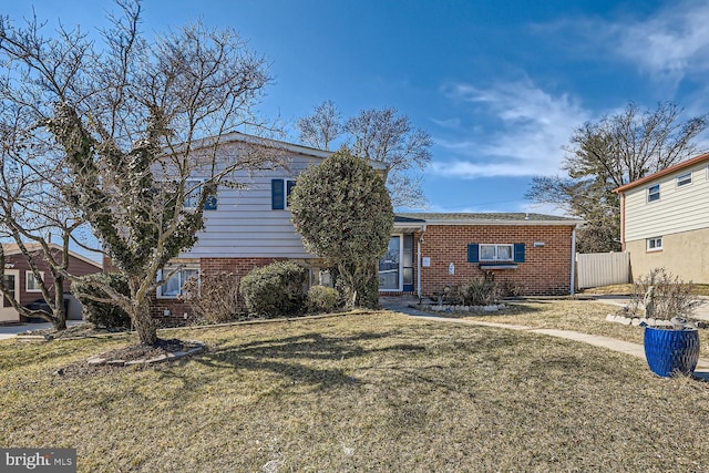 tri-level home with a front yard, brick siding, and fence