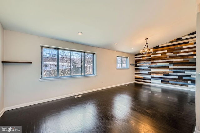 unfurnished living room with visible vents, baseboards, wood finished floors, vaulted ceiling, and a notable chandelier