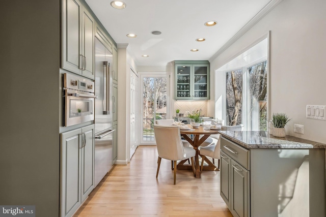 kitchen featuring gray cabinetry, glass insert cabinets, light wood-style floors, appliances with stainless steel finishes, and crown molding