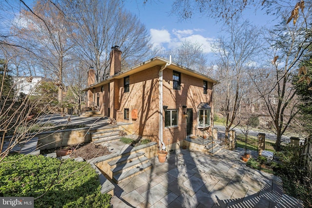 view of side of property with brick siding, a chimney, and fence