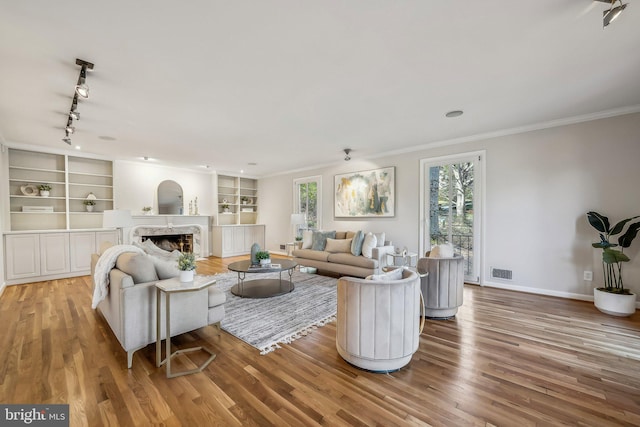 living area with visible vents, a fireplace, crown molding, and wood finished floors