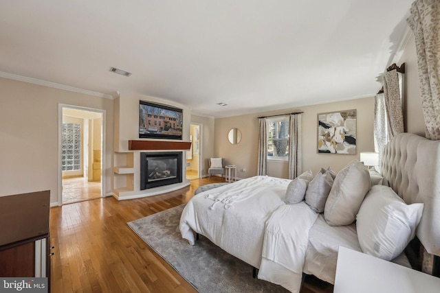 bedroom with visible vents, ornamental molding, a glass covered fireplace, wood-type flooring, and baseboards