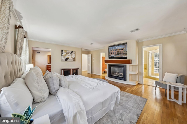 bedroom with visible vents, light wood-type flooring, a glass covered fireplace, and ornamental molding