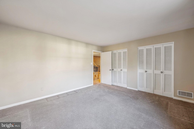 unfurnished bedroom with carpet, visible vents, two closets, and baseboards