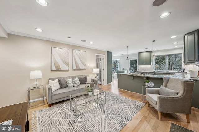 living area with recessed lighting, a healthy amount of sunlight, light wood finished floors, and ornamental molding