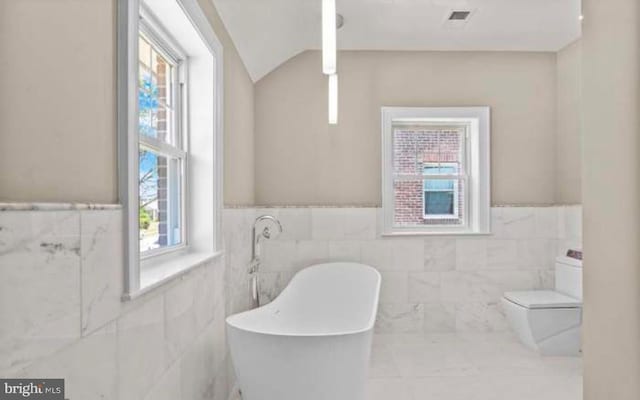 bathroom with visible vents, toilet, a wainscoted wall, a freestanding tub, and tile walls