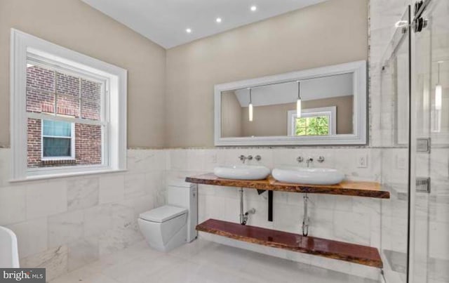 full bathroom with toilet, a stall shower, a sink, and tile walls