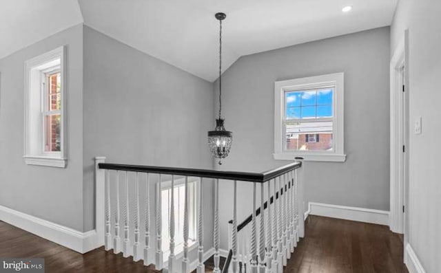 hall with baseboards, wood finished floors, vaulted ceiling, an upstairs landing, and a notable chandelier