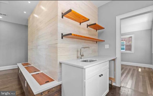 kitchen with dark wood-style floors, backsplash, white cabinets, a sink, and baseboards