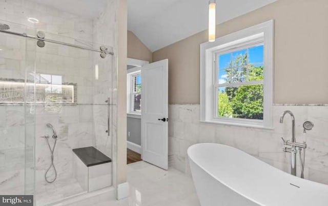 bathroom featuring a marble finish shower, lofted ceiling, a soaking tub, a wainscoted wall, and tile walls